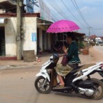 Většina žen a dívek jezdí na motorce s deštníkem (proti slunci)
